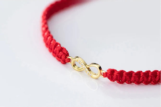 Detailansicht des vergoldeten Infinity-Symbols eingefügt in das handgeflochtene rote Kordelarmband.