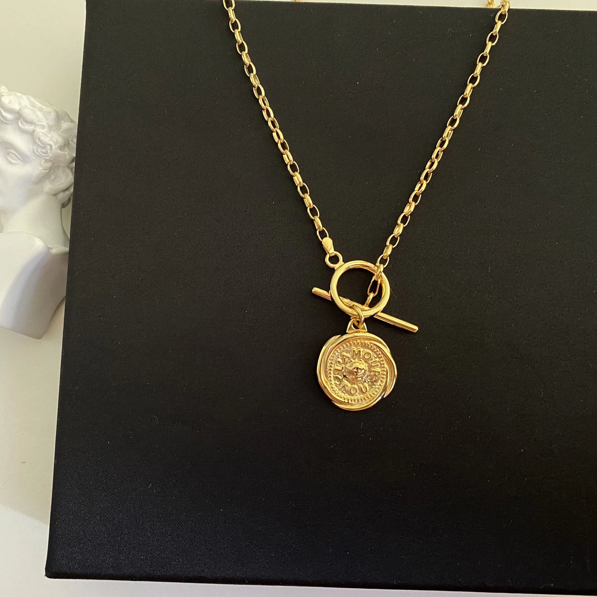 Produktansicht der 18K vergoldeten Messing-Kette mit Münzanhänger elegant präsentiert auf schwarzem Untergrund.
