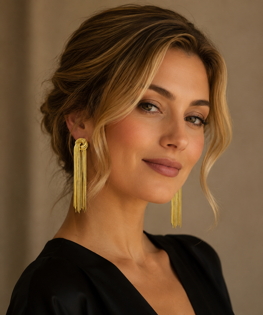 Eleganter Tragelook: Blonde Frau trägt lange, 18K vergoldete Titan-Ohrringe mit Knoten und feinen Ketten-Fransen.