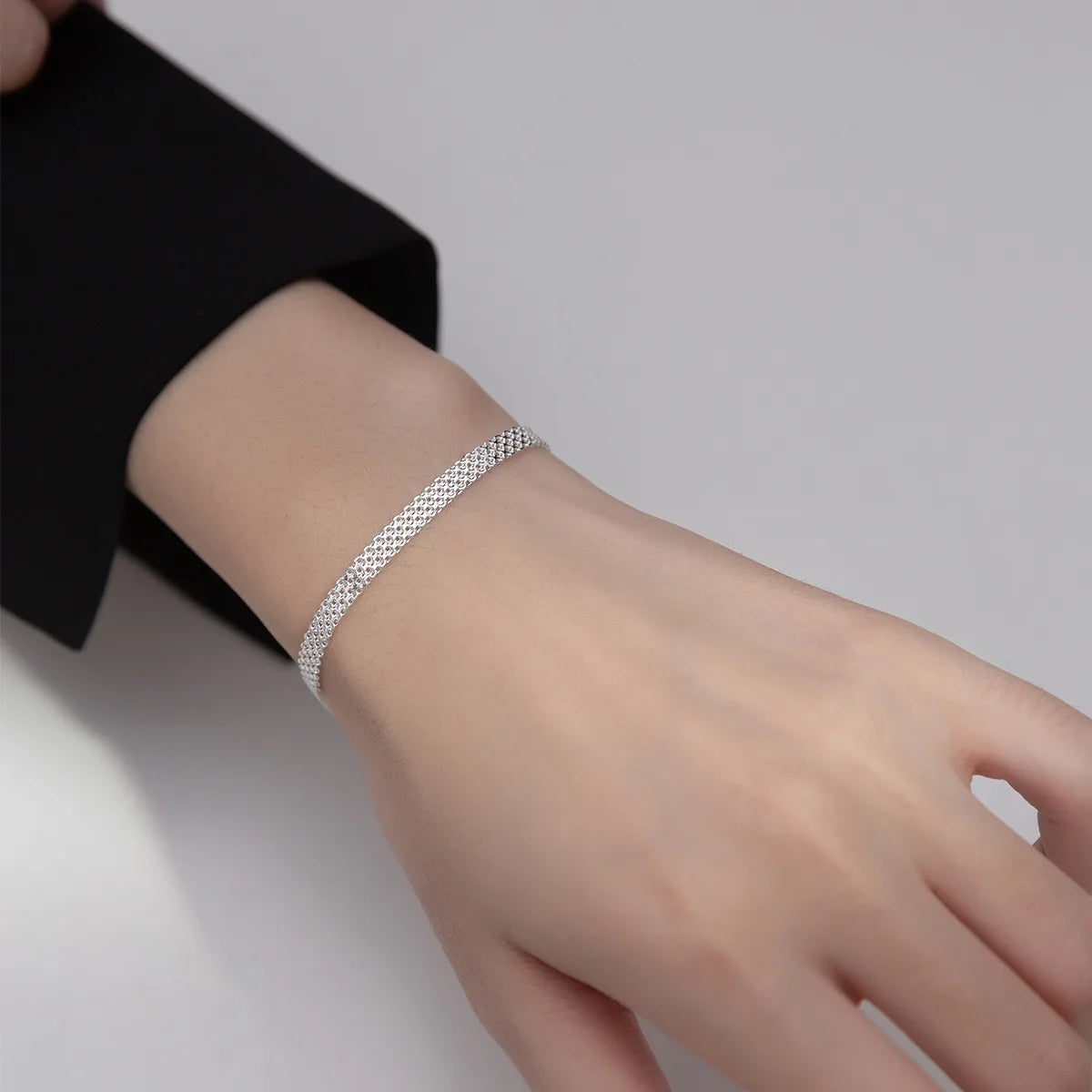 Elegantes Tragebild am Handgelenk: Silbernes Mesh-Gliederarmband zu einem schwarzen Blazer kombiniert