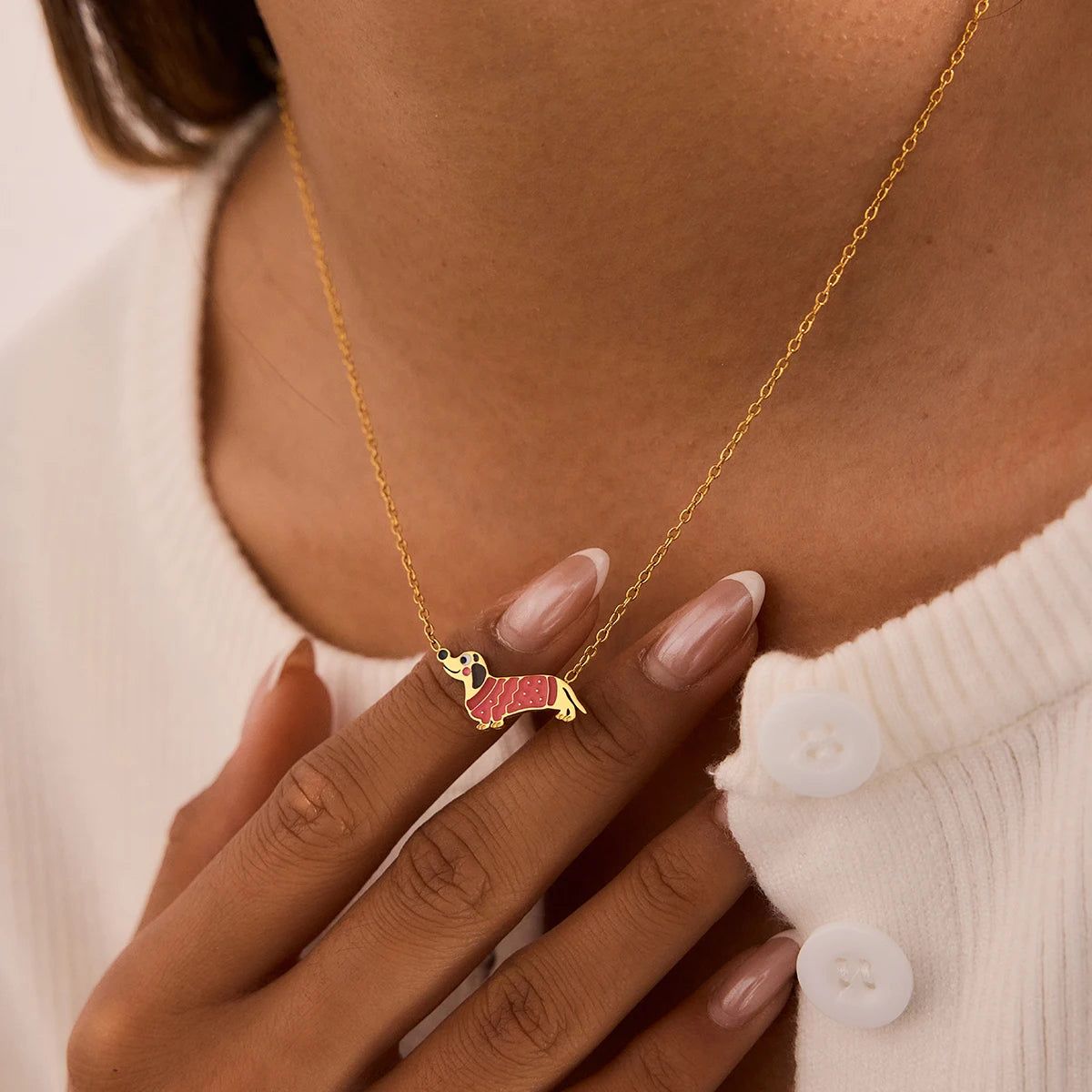 Eine Frau präsentiert die filigrane Dackel-Halskette aus 18K goldvergoldetem Edelstahl zu einem weißen Outfit.