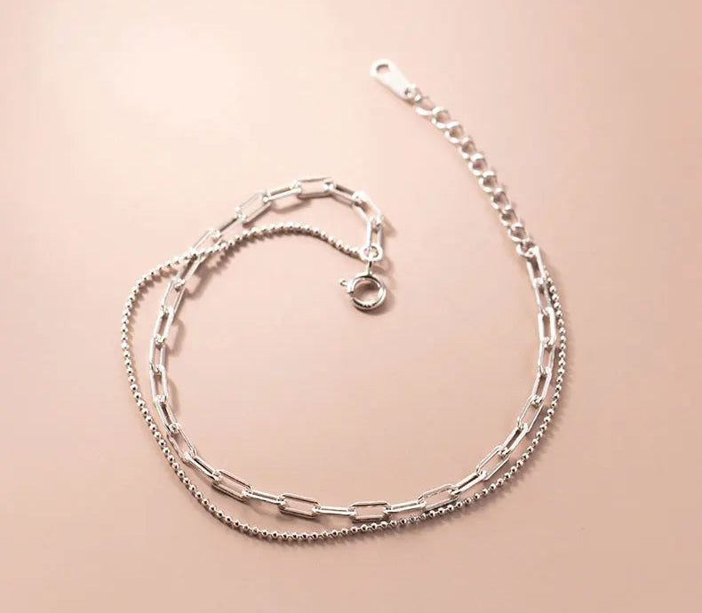 Produktansicht des zweireihigen Silberarmbands mit Karabiner- und Verlängerungskette auf warmem beigen Hintergrund