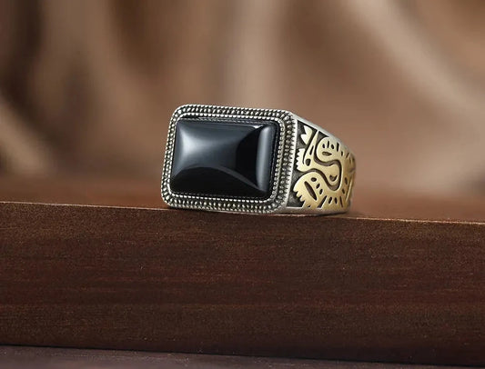Massiver Herrenring aus oxidiertem 925er Silber mit rechteckigem schwarzen Achat-Stein und goldenen Gravur-Details, platziert auf dunklem Holz.