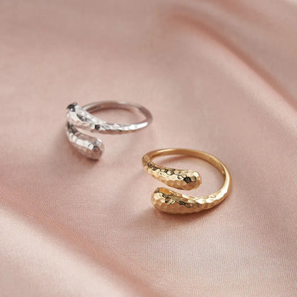 Silberner Schlangenring aus 925er Sterling und 14K Gold mit glatter Oberfläche, auf weichem rosa Stoff drapiert.