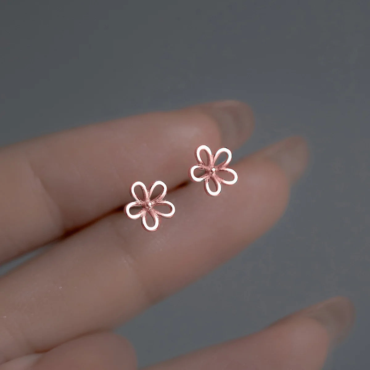 Produktfotografie der minimalistischen Blumen-Ohrstecker aus 925er Silber mit einer 18K Roségold Platierung auf einem dunklen Dekostein.