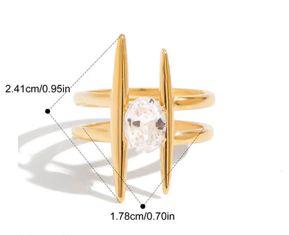 Grafische Darstellung eines goldenen Rings mit 18K PVD-Vergoldung. Er hat ein lineares, sich kreuzendes Design  und ist mit einem großen, klaren Zirkonia Stein besetzt. Die Maße sind ebenfalls angegeben mit einem Innendurchmesser von 1,8 cm und einer Breite von 2,4 cm.