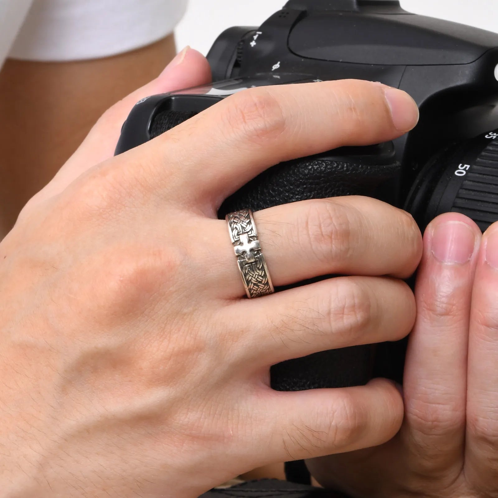 Detailaufnahme einer Hand, die eine Kamera hält und dabei den silberfarbenen Edelstahl-Ring mit Kreuz-Muster am Finger zeigt.