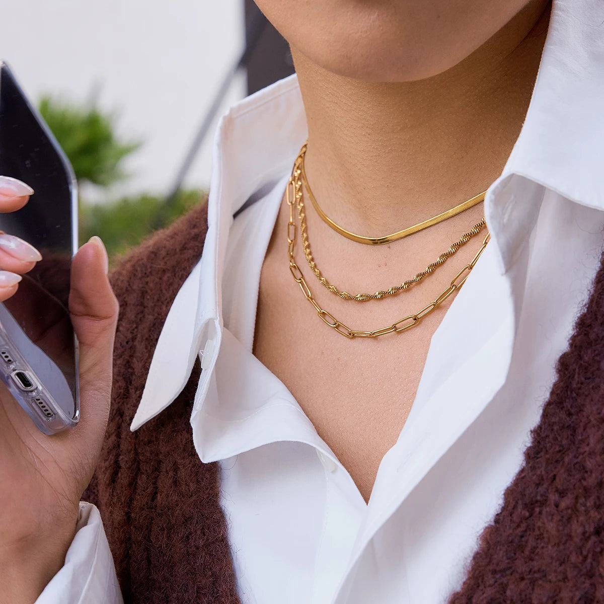 Model präsentiert ein dreireihiges, goldenes Ketten-Set aus Edelstahl und 18K Gold im Layering-Look über einer weißen Bluse.