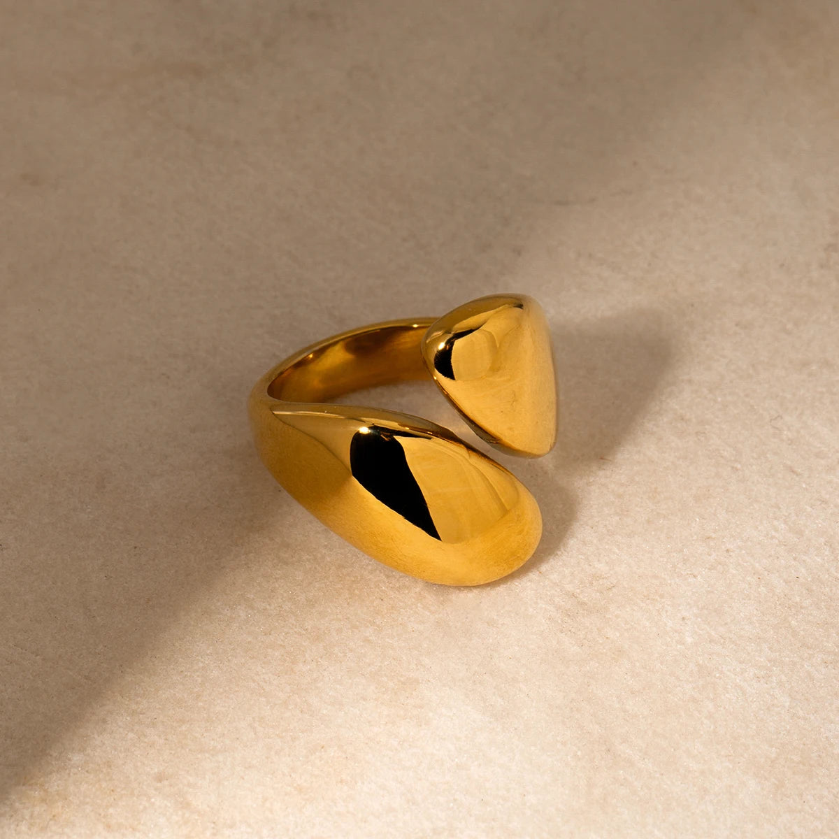 Elegantes Stillleben-Foto des gold vergoldeten Edelstahlrings auf einem hellen Steingut-Hintergrund, das das skulpturale, offene Design aus einem anderen Blickwinkel betont.