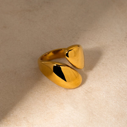 Elegantes Stillleben-Foto des gold vergoldeten Edelstahlrings auf einem hellen Steingut-Hintergrund, das das skulpturale, offene Design aus einem anderen Blickwinkel betont.
