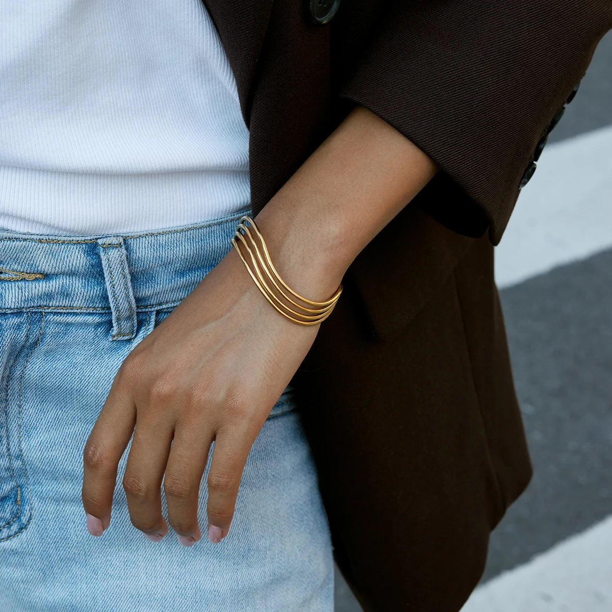 Casual-Business-Look: Breit gefächerter goldener Edelstahl-Armreif kombiniert mit Jeans und weißem Shirt.