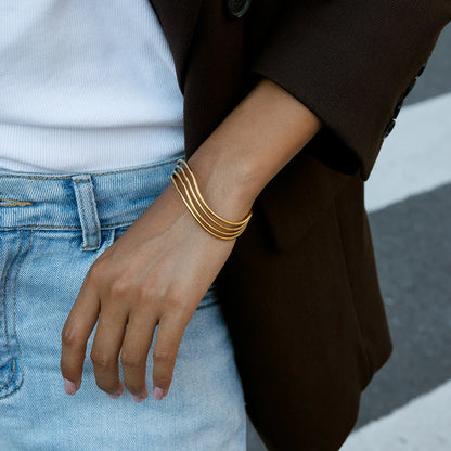 Casual-Business-Look: Breit gefächerter goldener Edelstahl-Armreif kombiniert mit Jeans und weißem Shirt.