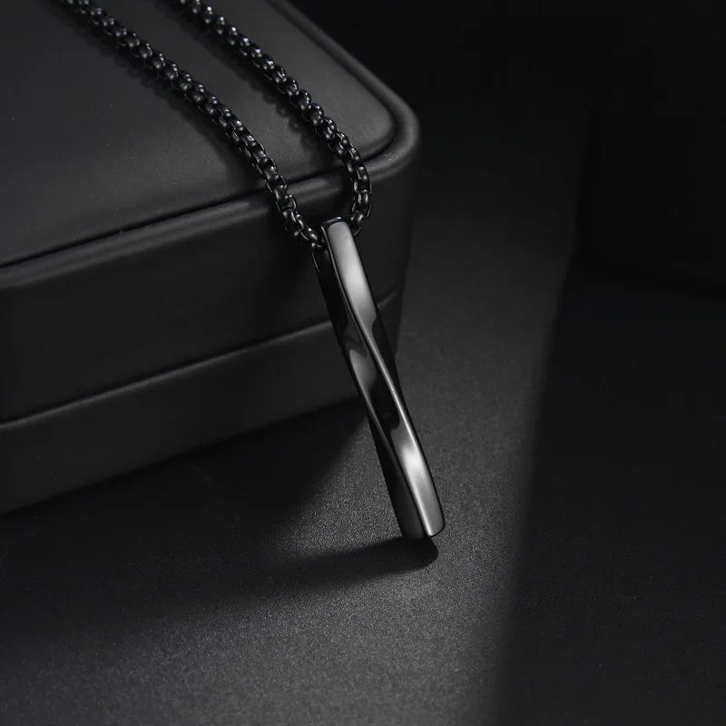  Schwarze Edelstahl-Kette mit einem verdrehten Stab-Anhänger auf einem dunklen und hellen Hintergrund.