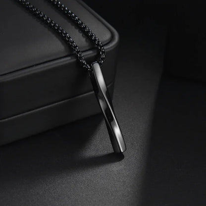  Schwarze Edelstahl-Kette mit einem verdrehten Stab-Anhänger auf einem dunklen und hellen Hintergrund.