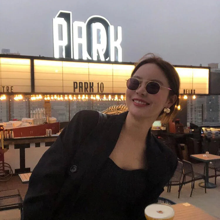 Model trägt kleine, klobige 18K vergoldete Creolen, sitzt lächelnd vor einem Café-Schild.