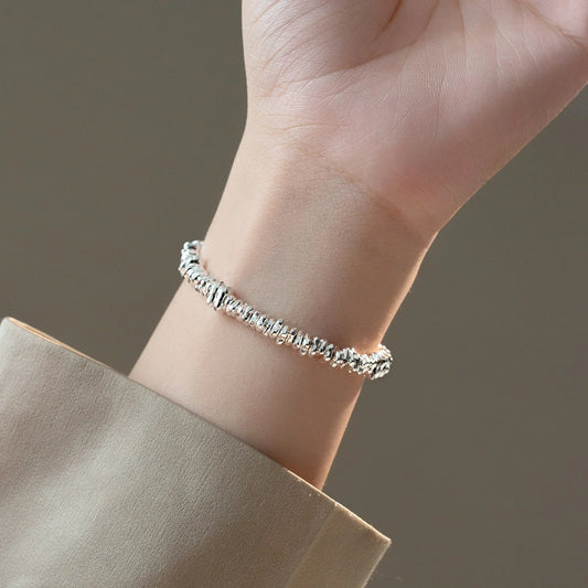 Eine Frau trägt das Armband mit den "zerknüllten" 925er Silber-Elementen am Handgelenk, wobei ein Teil eines beigefarbenen Ärmels sichtbar ist.