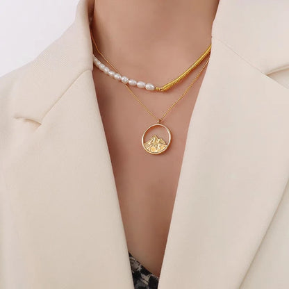 Stylischer Layering-Look: Asymmetrische Perlen- und Schlangenkette kombiniert mit einer zweiten goldenen Medaillon-Halskette zu einem weißen Blazer.