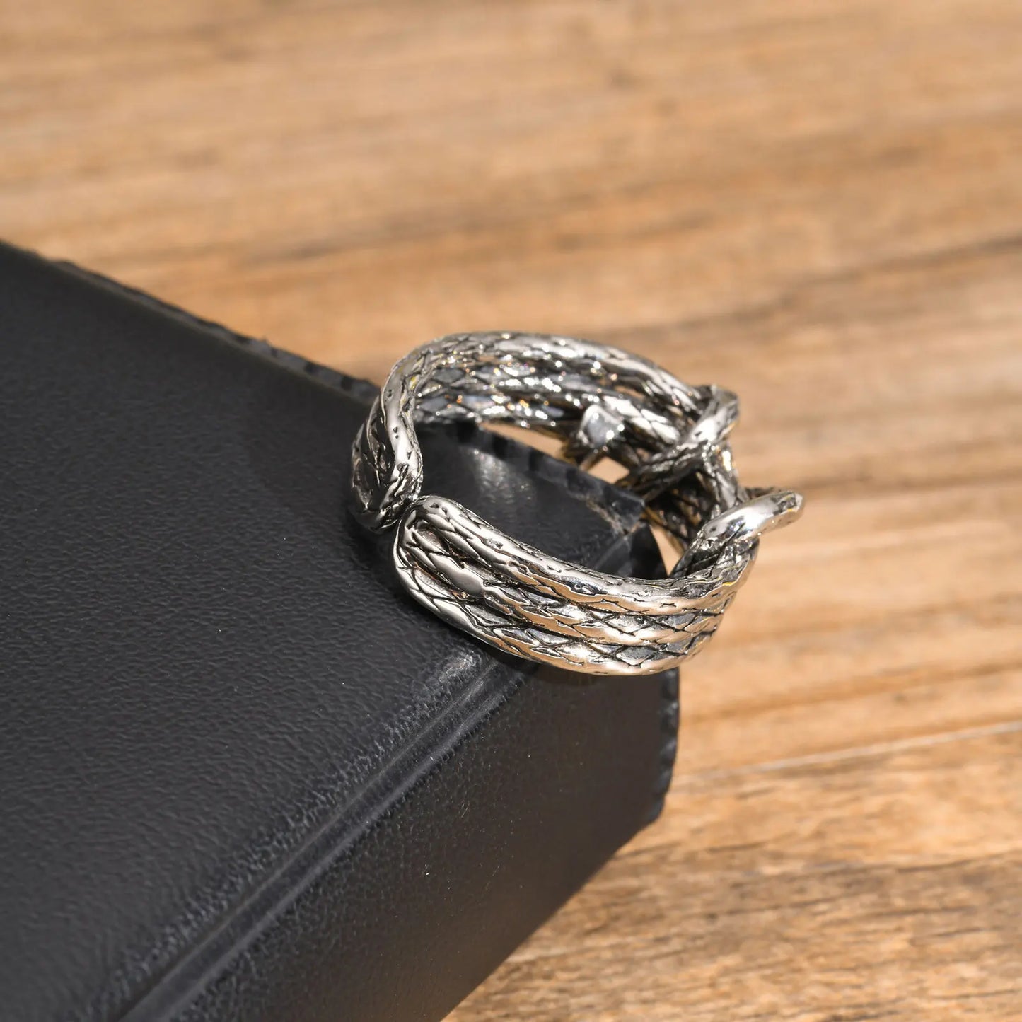 Der offene Edelstahl-Knotenring liegt schräg auf einer schwarzen Oberfläche.