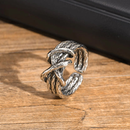 Breiter, offener Edelstahl-Ring im gedrehten Seil- oder Knoten-Design (Tauwerk-Muster), liegend auf einem Holzuntergrund, um das rustikale, oxidierte Silber-Finish hervorzuheben.
