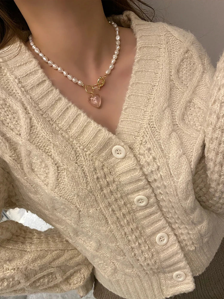Naturperlenkette mit vergoldetem Titan-Knebelverschluss und altrosafarbenem Herz-Anhänger zu einem beigen Cardigan.