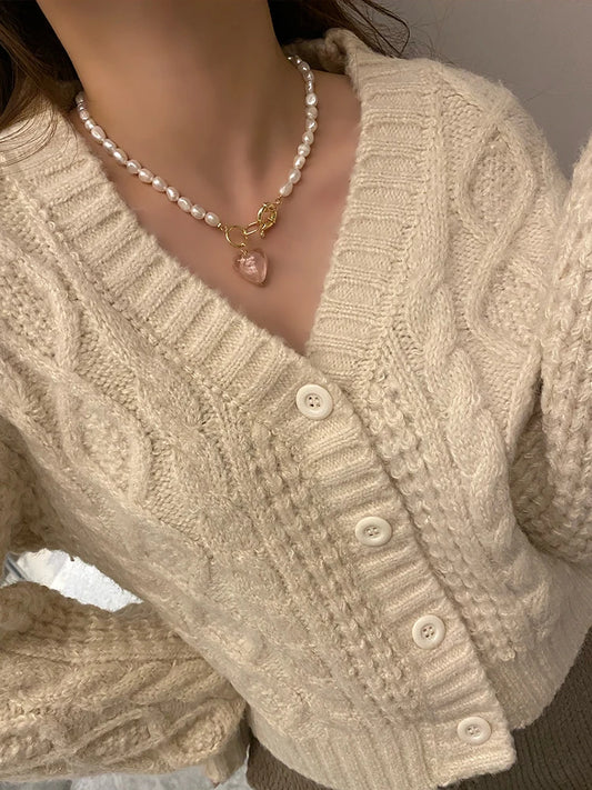 Naturperlenkette mit vergoldetem Titan-Knebelverschluss und altrosafarbenem Herz-Anhänger zu einem beigen Cardigan.