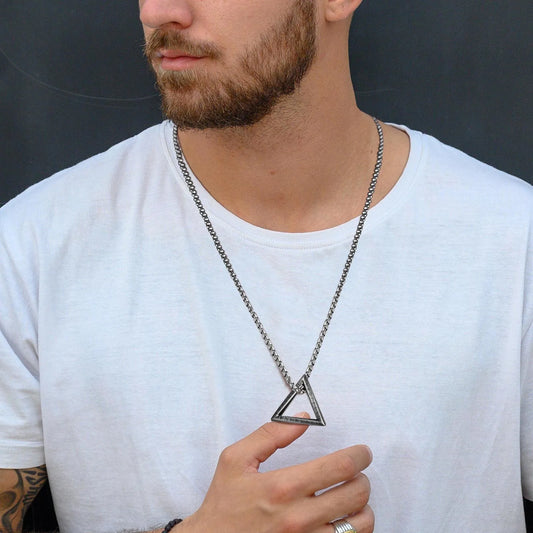 Edelstahlkette mit dreieckigem, offenem Anhänger getragen von einem Mann mit Bart über einem weißen T-Shirt.