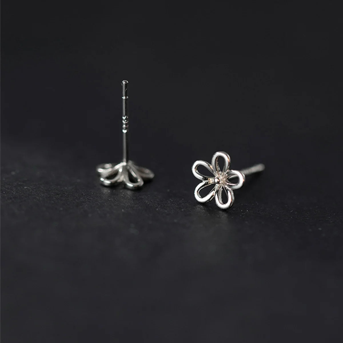 Filigrane blütenförmige Ohrstecker aus 925er Silber mit 18K Roségold-Plattierung sanft auf Fingerspitzen präsentiert.   