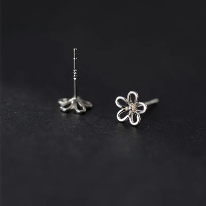 Filigrane blütenförmige Ohrstecker aus 925er Silber mit 18K Roségold-Plattierung sanft auf Fingerspitzen präsentiert.   
