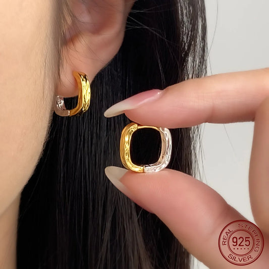 Nahaufnahme vom Ohr einer Frau mit gehämmerten, zweifarbigen Huggie-Creolen aus 925er Silber und 18K Vergoldung.