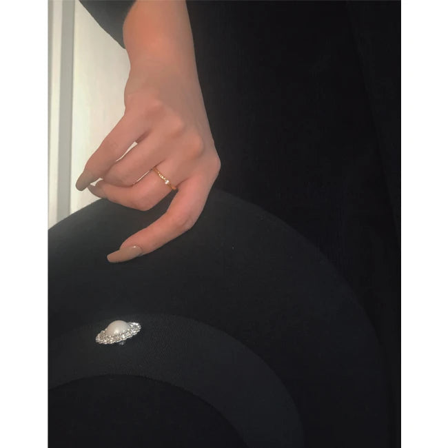 Tragestyling: Hand mit filigranem vergoldetem Zirkonia-Ring über einem schwarzen Hut.