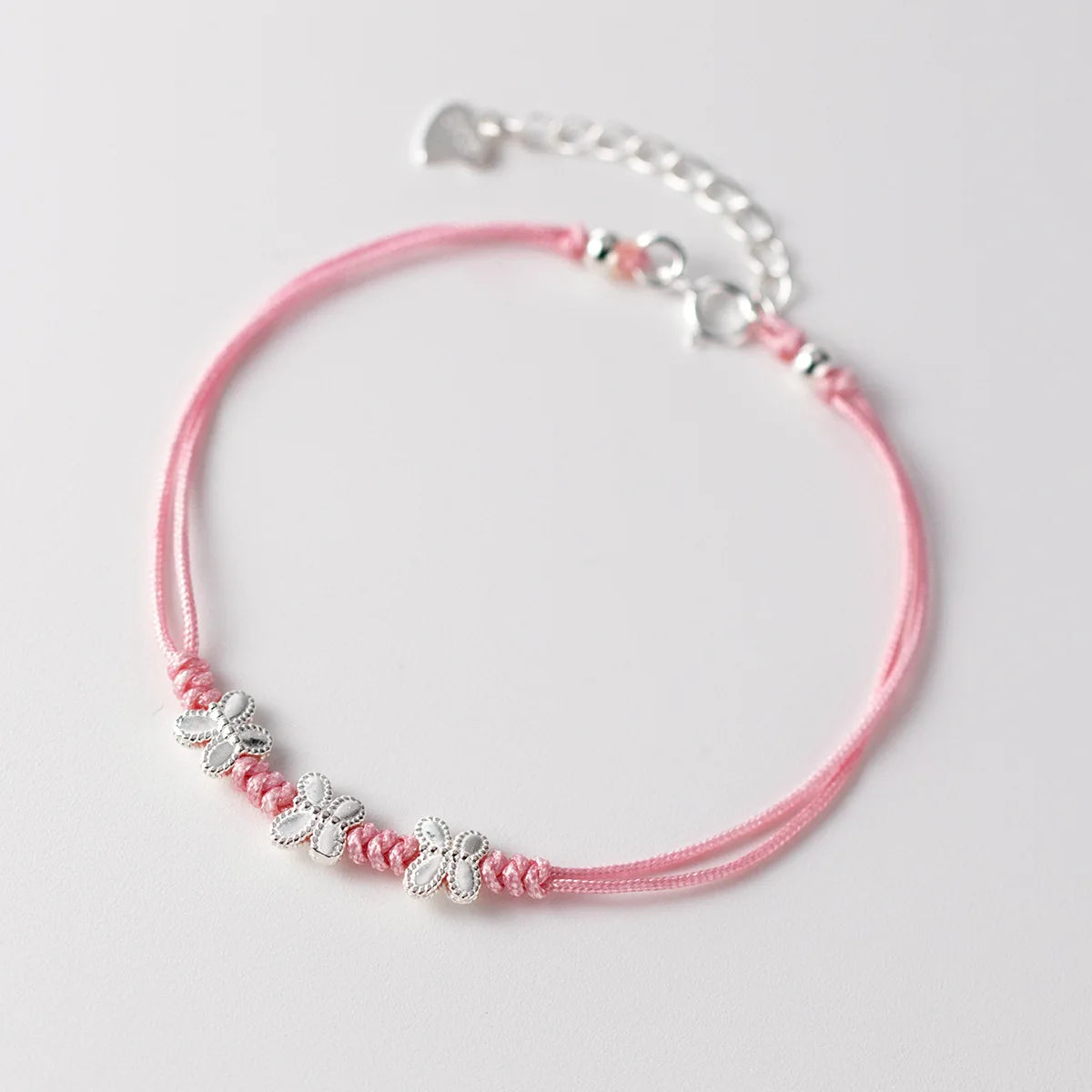 Rosa Ausführung des feinen Textilarmbands mit drei filigranen Schmetterlingen aus 925er Silber auf hellem Untergrund.