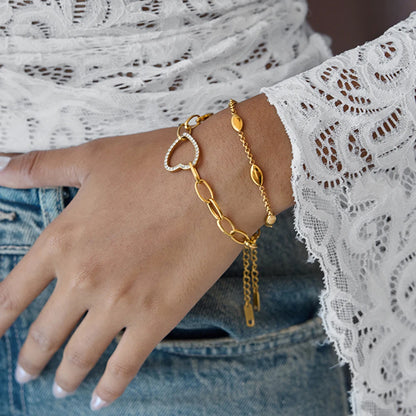 Stilvoller Armband-Layering-Look: Vergoldetes Zirkonia-Herz-Armband kombiniert mit einer weiteren Goldkette am Handgelenk