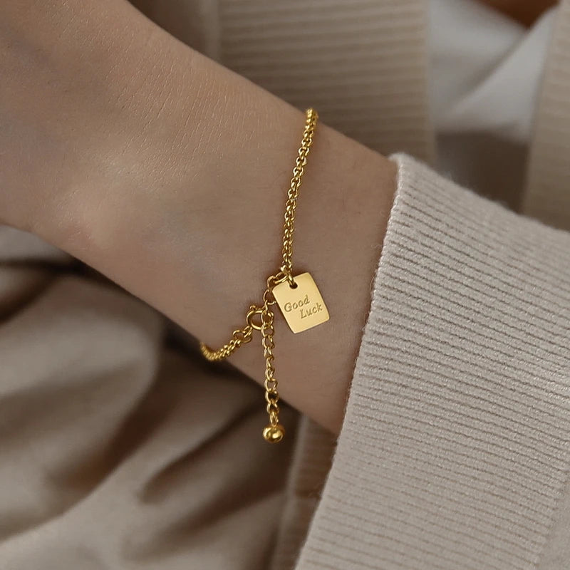 Vergoldetes Gliederketten-Armband aus Titan mit einem rechteckigen Plättchen-Anhänger („Good Luck“).