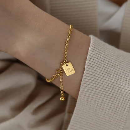 Vergoldetes Gliederketten-Armband aus Titan mit einem rechteckigen Plättchen-Anhänger („Good Luck“).