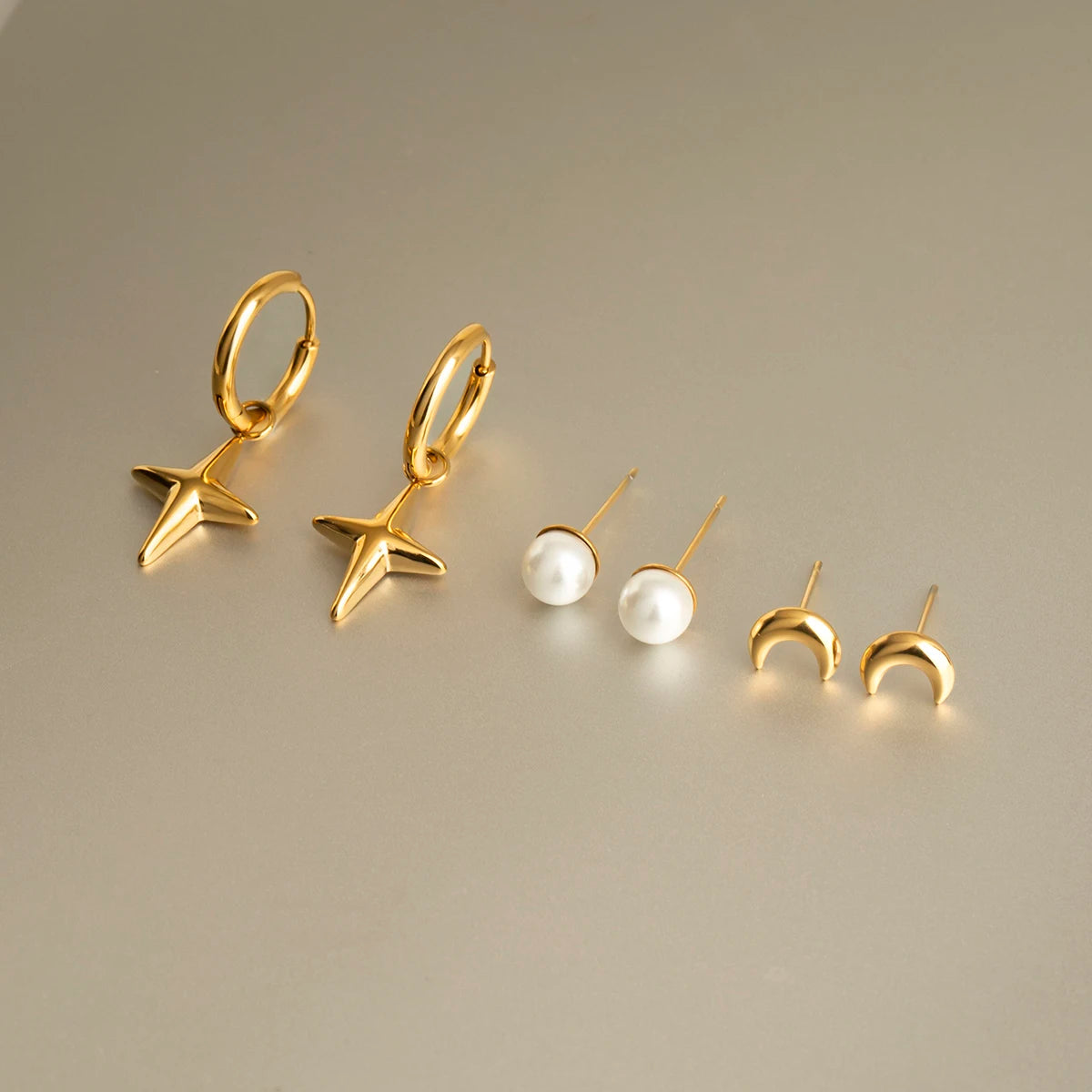 Ein Set aus sechs kleinen goldenen Edelstahl-Ohrsteckern und Kreolen-Ohrringen mit 18K PVD-Vergoldung. Die Designs umfassen einen hängenden Stern, einen einzelnen Stern, einen Halbmond, eine schlichte Kugel, einen Tropfen und eine einfache kleine Kreole.