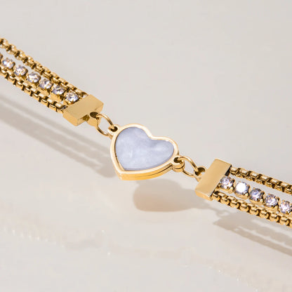Nahaufnahme des filigranen Schmuckstücks: Mehrreihiges goldenes Strassarmband mit einem schimmernden Herz-Inlay, diagonal fotografiert.