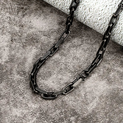Nahaufnahme der schwarzen, matten Edelstahl-Gliederkette. Der Fokus liegt auf der Vintage-Textur der dicken, rechteckigen Kettenglieder, liegend auf einem dunklen, steinernen Untergrund.