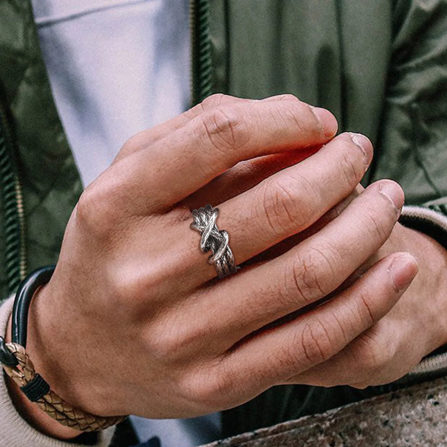 Nahaufnahme eines Mannes mit Lederarmband, der den offenen Edelstahl-Knotenring am Finger trägt.