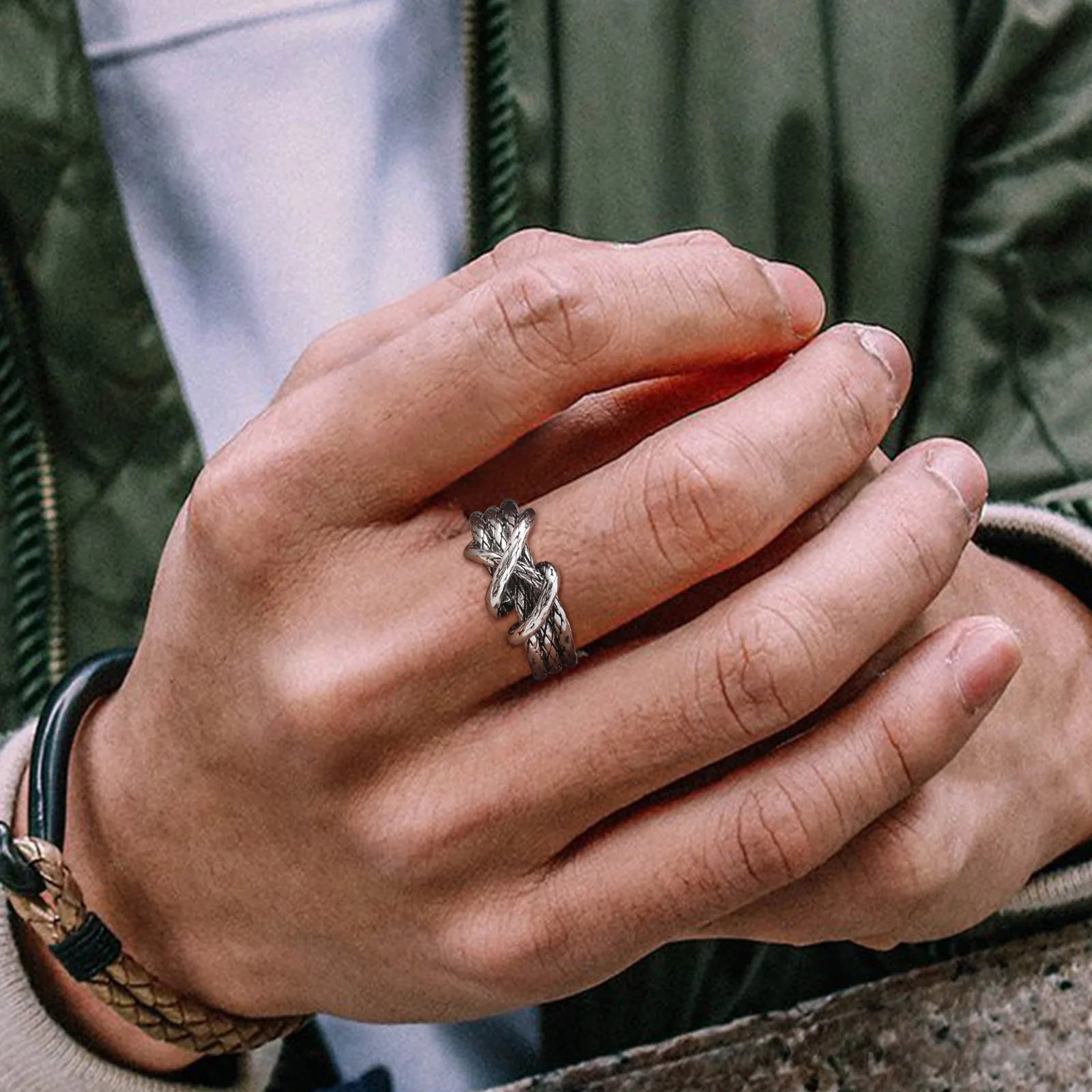 Nahaufnahme eines Mannes mit Lederarmband, der den offenen Edelstahl-Knotenring am Finger trägt.