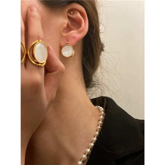 Modernes Schmuck-Ensemble: Eine Frau trägt die runden Perlmutt-Ohrringe und den passenden Statement-Ring zu einer eleganten Perlenkette.