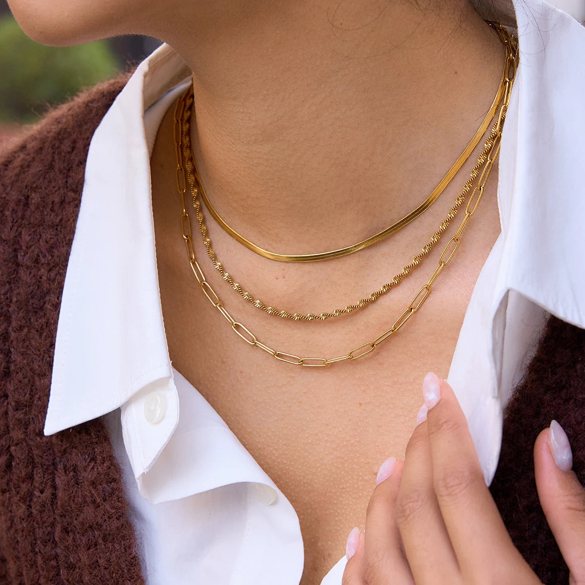 Nahaufnahme einer Frau mit einem mehrreihigen, goldenen Edelstahl-Halsketten-Set aus 18K Gold mit Fischgrät-, Kordel- und Paperclip-Kette.