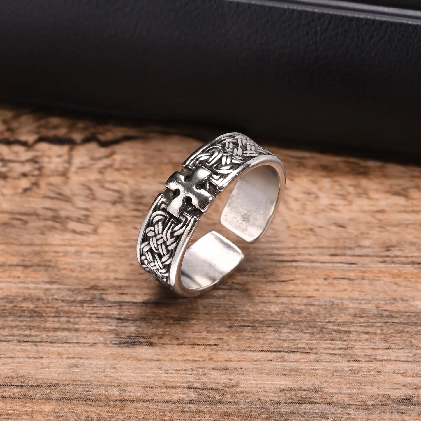 Freigestellte Ansicht des breiten, silberfarbenen Edelstahl-Rings mit detailliertem Kreuz-Muster, liegend auf einem Holzuntergrund.