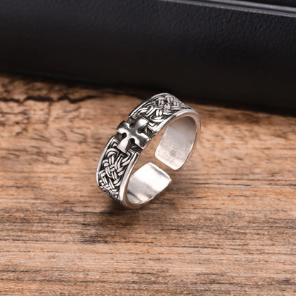 Freigestellte Ansicht des breiten, silberfarbenen Edelstahl-Rings mit detailliertem Kreuz-Muster, liegend auf einem Holzuntergrund.