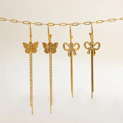 Produktübersicht der Kollektion: Vier unterschiedliche, lange Ohrhänger aus vergoldetem Edelstahl mit Schmetterlings- und Schleifen-Motiven, aufgereiht an einer goldenen Gliederkette.