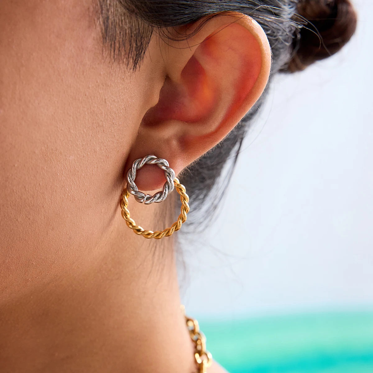 Rückansicht des Ohrs einer Person, die einen Ohrring aus zwei ineinandergreifenden Ringen trägt. Der obere Ring ist goldfarben, der untere ist silberfarben.