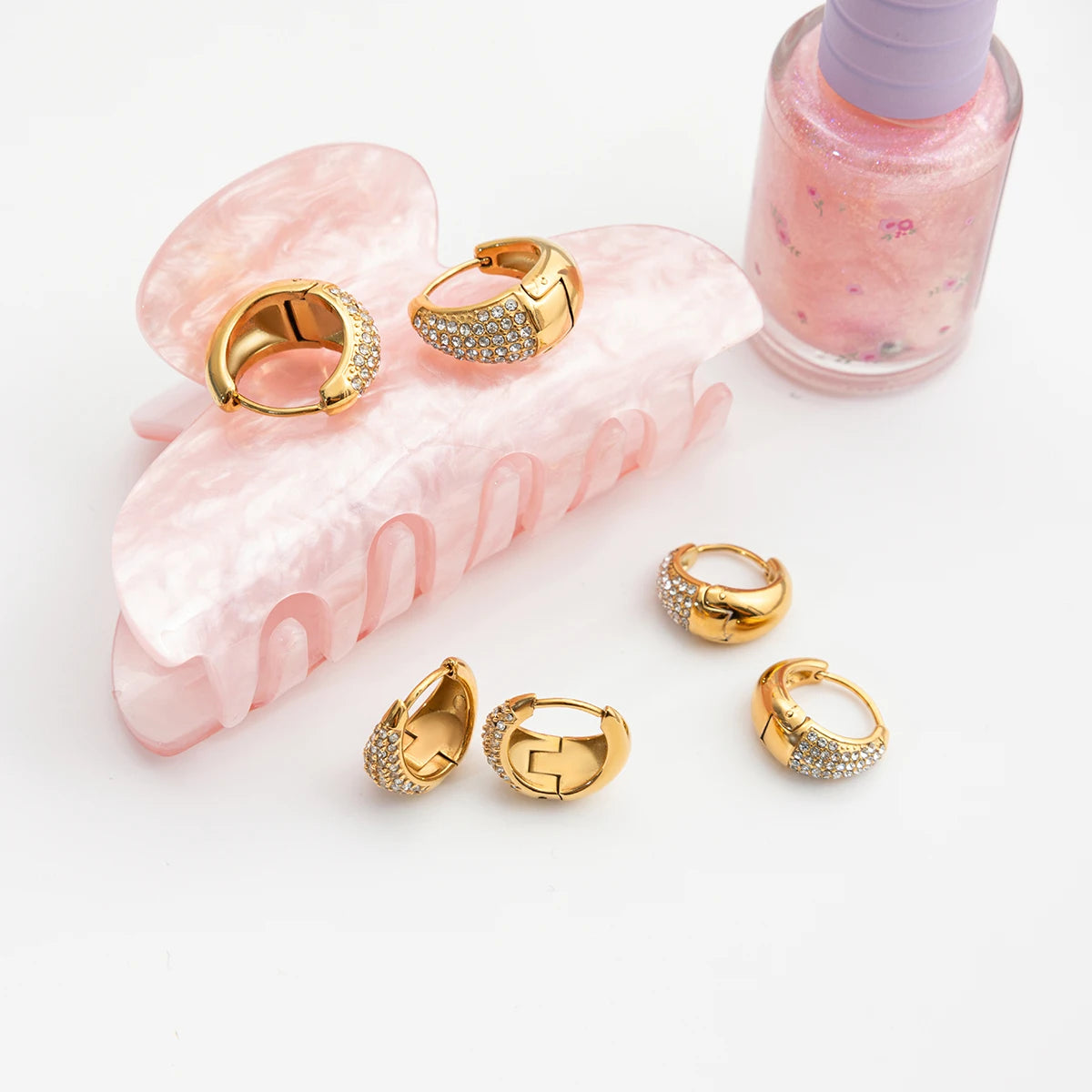 „Goldene Zirkonia-Ohrringe kombiniert mit einer Haarspange und Nagellack, modernes Schmuckdesign aus langlebigem Edelstahl.“