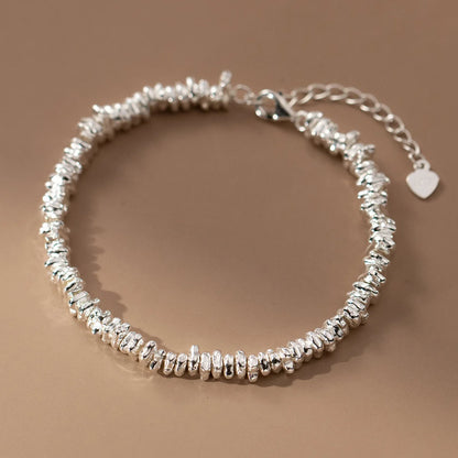 Draufsicht auf das Armband aus 925er Silber mit den unregelmäßigen Elementen, das in einer geschlossenen Kreisform auf einer hellbraunen Oberfläche liegt.