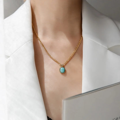 „Nahaufnahme einer Frau, die eine mittellange goldene Kette mit einem ovalen, türkisblauen Anhänger über einem schwarzen Top trägt.“