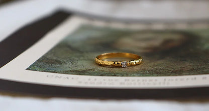 Filigraner 18K vergoldeter Zirkonia-Ring aus Messing auf einem aufgeschlagenen Kunstmagazin.