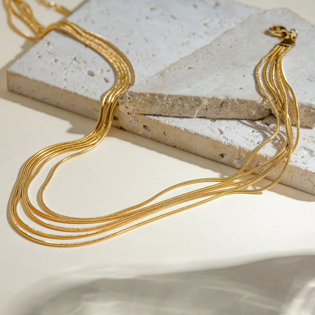 5-reihige goldene Schlangenkette aus Edelstahl auf einer beigefarbenen Steinplatte